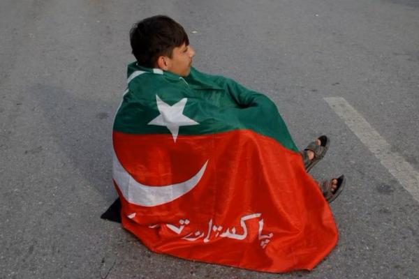 Seorang pendukung partai mantan Perdana Menteri Pakistan Imran Khan, Pakistan Tehreek-e-Insaf terbungkus bendera partai, duduk di jalan di Peshawar, Pakistan, 12 Februari 2024. Foto: Reuters 