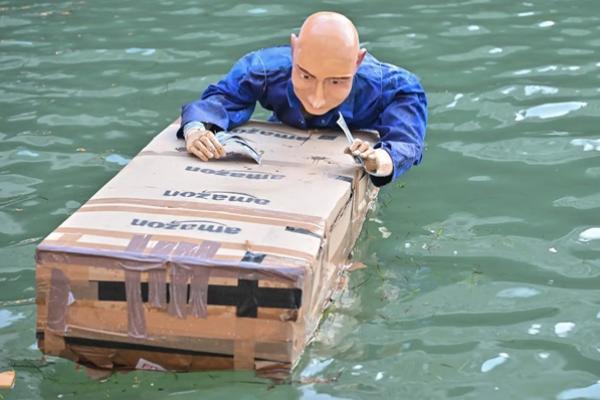 Boneka Jeff Bezos mengapung di kanal Venesia sambil berpegangan pada kotak dan uang tunai Amazon. (FOTO: SHUTTERSTOCK) 