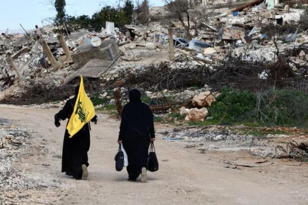 Wanita berjalan di dekat bangunan yang hancur, dengan satu orang memegang bendera Hizbullah, di desa Kfar Kila di Lebanon selatan, 18 Februari 2025. REUTERS 