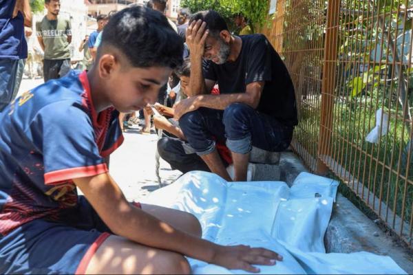 Seorang pria Palestina bersama putranya, berduka di samping jenazah putranya yang lain, yang tewas akibat tembakan Israel saat mencari bantuan di dekat titik distribusi di Rafah, di Rumah Sakit Nasser, Khan Younis, Jalur Gaza selatan, 12 Juli 2025. REUTERS 