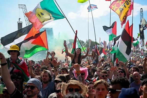 Para pengunjung yang membawa bendera Palestina dan bendera lainnya berkumpul saat Kneecap tampil di Festival Glastonbury di Worthy Farm di Pilton, Somerset, Inggris, 28 Juni 2025. (FOTO: REUTERS) 