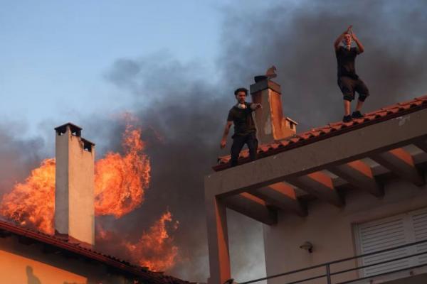 Warga berteriak dari atap rumah saat api membubung dari sebuah rumah yang terbakar, di desa Kryoneri, dekat Athena, Yunani, 26 Juli 2025. REUTERS 