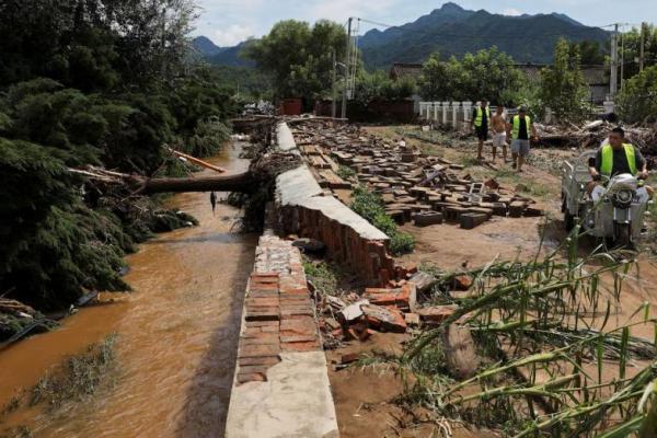 Orang-orang berjalan melewati pohon-pohon tumbang dan tanaman jagung yang rusak, setelah hujan deras membanjiri daerah tersebut di distrik Miyun, Beijing, Tiongkok, 29 Juli 2025. REUTERS 
