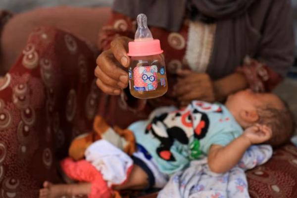 Nemah Hamouda memegang botol susu bayi sambil menggendong cucunya yang berusia tiga bulan, Muntaha, di Kota Gaza, 29 Juli 2025. REUTERS 