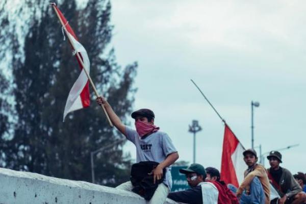 Seorang demonstran mengibarkan bendera merah putih (Foto: Unsplash/andrie chassidy) 