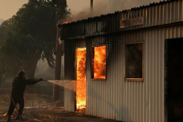 Seorang petugas pemadam kebakaran berupaya memadamkan api dari sebuah bangunan saat terjadi kebakaran hutan di Sichaina, dekat Patras, Yunani, 13 Agustus 2025. (FOTO: REUTERS)  