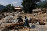 Seorang warga berjalan melewati puing-puing kendaraan yang tersangkut di antara bebatuan dan batu besar, di wilayah Qadir Nagar, distrik Buner, provinsi Khyber Pakhtunkhwa, Pakistan, 21 Agustus 2025. REUTERS