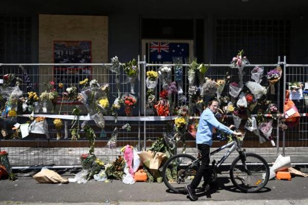 Seorang anak laki-laki bersepeda melihat di samping karangan bunga dan bendera Australia di Sinagoge Adass Israel setelah serangan di Melbourne, Australia, 10 Desember 2024. AAP via REUTERS 
