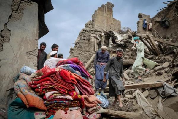 Pria-pria Afghanistan berjalan di atas reruntuhan rumah yang rusak akibat gempa bumi berkekuatan 6,0 skala Richter yang melanda Afghanistan pada hari Minggu, di Mazar Dara, Provinsi Kunar, Afghanistan. (FOTO: REUTERS) 