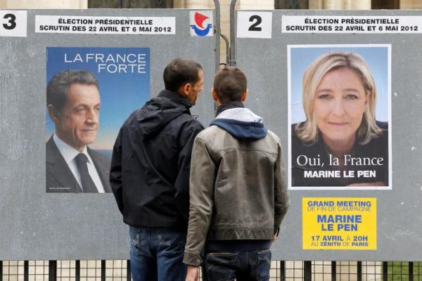 Orang-orang berhenti untuk membaca poster kampanye resmi untuk para kandidat dalam pemilihan presiden Prancis: Nicolas Sarkozy dan Marine Le Pen, di Paris, 9 April 2012. REUTERS 