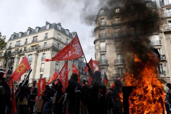 Demonstran yang membawa bendera berjalan melewati tempat sampah yang terbakar selama demonstrasi di Paris sebagai bagian dari aksi mogok nasional dan protes terhadap pemerintah dan kemungkinan pemotongan anggaran di Prancis, 2 Oktober 2025. REUTERS 