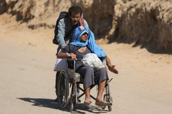 Seorang warga Palestina membantu seorang pria di kursi roda membawa barang-barangnya saat warga Palestina yang mengungsi dari Gaza utara akibat operasi militer Israel, di Jalur Gaza tengah, 2 Oktober 2025. REUTERS 