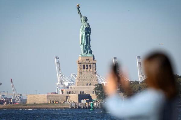 Seorang perempuan memotret Patung Liberty dari Battery Park pada hari pertama penutupan sebagian pemerintah AS di New York City, New York, AS, 1 Oktober 2025. REUTERS 