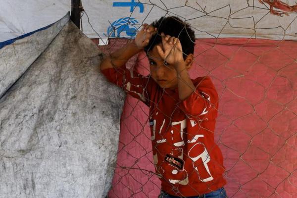 Seorang anak Palestina yang mengungsi akibat operasi militer Israel, berdiri di dekat pagar, sambil beristirahat di pinggir jalan, di Jalur Gaza tengah, 5 Oktober 2025. REUTERS 