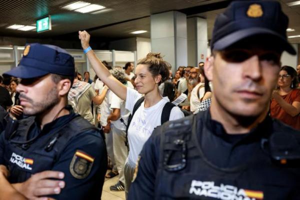 Salah satu aktivis Spanyol yang merupakan bagian dari Armada Sumud Global dan ditahan oleh pasukan Israel, memberi isyarat di samping petugas polisi saat tiba di Bandara Adolfo Suarez Madrid-Barajas di Madrid, Spanyol, 5 Oktober 2025. REUTERS 