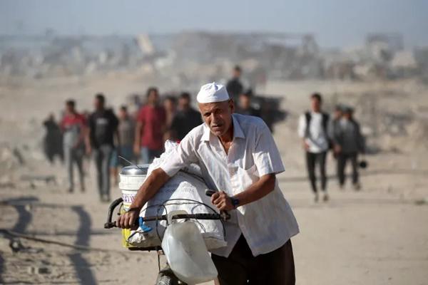 Seorang pria mendorong sepedanya saat warga Palestina berjalan menuju Kota Gaza dari Nuseirat di Gaza tengah pada 11 Oktober 2025. (FOTO: AFP) 