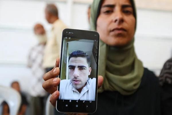 Ghada Musbeh sedang berusaha menemukan suaminya di antara jenazah-jenazah yang dibebaskan Israel. Ia mengangkat ponselnya yang berfoto dengan suaminya di Khan Younis, Gaza, 16 Oktober 2025. (FOTO: REUTERS) 